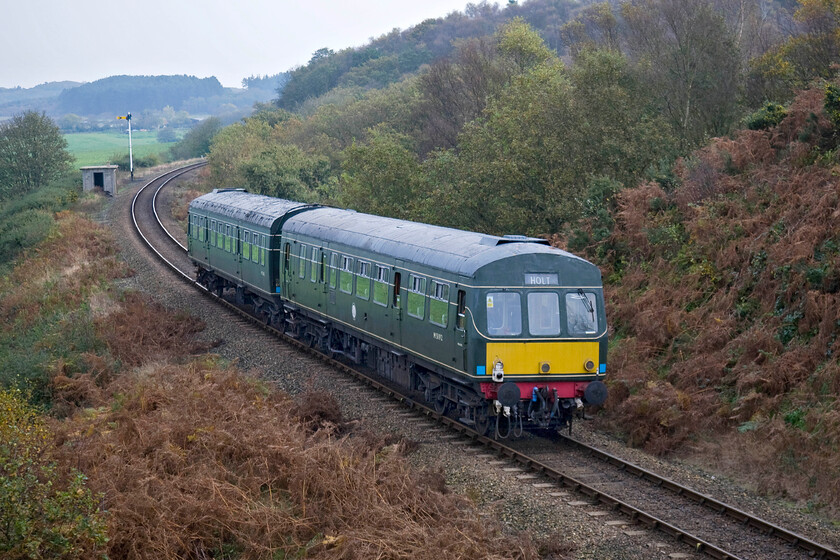 M51192 & M56352, 10.30 Holt-Sheringham, Kelling bank 
 At one of my favourite spots on the North Norfolk Railway just over halfway up Kelling bank, M51192 leads M56352 working the first service of the day, the 10.30 Holt to Sheringham. Note the tail light attached o the rear of the Class 101 DMU indicating that this is in fact a going away photograph! Just out of view around the curve in the trees, the DMU will pause at the diminutive Kelling Heath halt. 
 Keywords: M51192 M56352 10.30 Holt-Sheringham Kelling bank Class 101 DMU