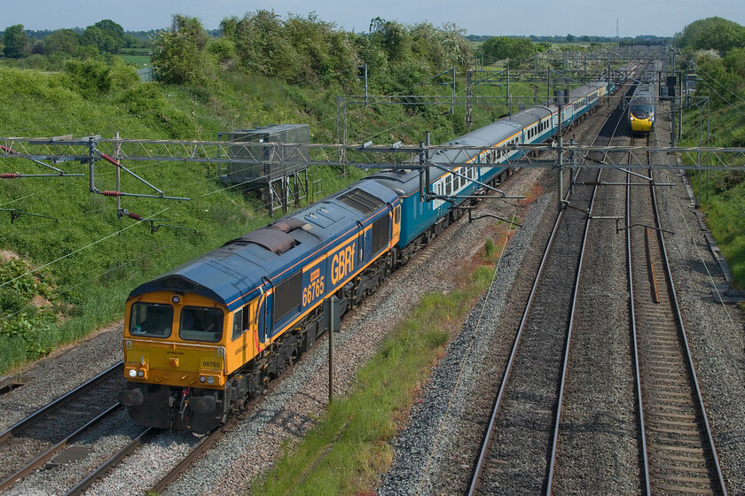 66765, 14.20 Wembley Reception-Burton-ot-Wetmore (5Z68, 3L) & 390020, VT 14.52 London Euston-Manchester Piccadilly (1H27, 15L), Victoria bridge 
 On a perfect spring afternoon, 66765 'Julie Garn' leads the 14.20 Wembley Reception to Burton-ot-Wetmore empty coaching stock move. The previous day the stock and locomotives had been used to operate The Parkeston Panorama charter from London to Norwich via a roundabout route including, as the name suggests, a return run down the Harwich branch via Parkstone Quay. This Class 66 was named last year (2022) in a short ceremony at Great Yarmouth in recognition of another member of the GBRf team, in this case, their international business leader. With AWC's 390020 approaching fast the scene is taken at Victoria bridge just south of Roade. 
 Keywords: 66765 14.20 Wembley Reception-Burton-ot-Wetmore 5Z68 390020 14.52 London Euston-Manchester Piccadilly 1H27 Victoria bridge Julie Garn