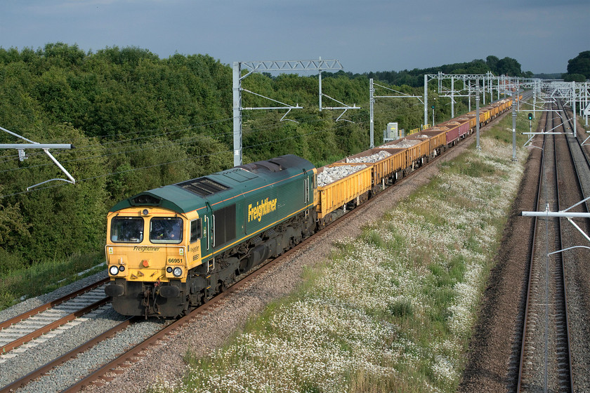 66951, 17.00 Crickelwood yard-Toton North yard (6Y75, 1L), Irchester SP927667 
 A very rare burst of sunshine unusually coincided with the passage of the 6Y75 17.00 Cricklewood to Toton North ballast working composed of a mixture of MLA and MJA wagons. Usually, the locomotive would just be in the shade with the trees in the background in full sun but today things came together! 66951 leads the train gingerly down Sharnbrook bank at Irchester on the down slow line under wiring that is still awaiting to be energised except for testing purposes. Notice the rust stains underneath the driver's window on the Class 66. This appears to be a common problem on a number of members of the class with the only probable rectification being the removal of the screen and seal with proper repairs then made to the seam that will be the one giving trouble. 
 Keywords: 66951 17.00 Crickelwood yard-Toton North yard 6Y75 Irchester SP927667 Freightliner MLA JLA