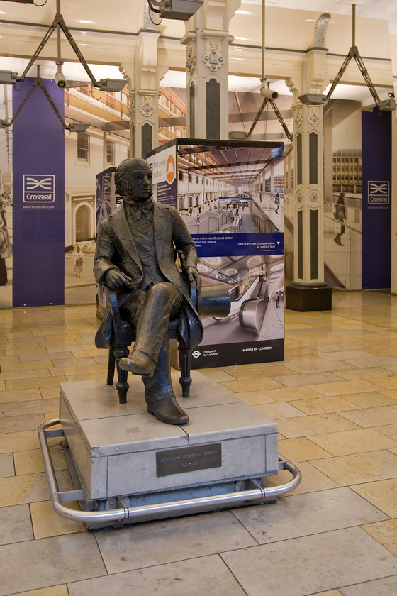 IKB statue & Crossrail exhibition, platform 1, Paddington station 
 At some time in the future, with the date becoming a moving feast, Crossrail 'may' open! If and when it does passengers will access Paddington's platforms through these ornate arches to the station below and behind. Indeed, the artist impressions on the display board illustrate what this will look like. IK Brunel sits patiently waiting for this opening but given the news emerging from Crossrail, despite their optimistic announcements and the TV programmes, indicates huge delays pushing opening back in terms of years rather than months! 
 Keywords: IKB statue Crossrail exhibition platform 1 Paddington station