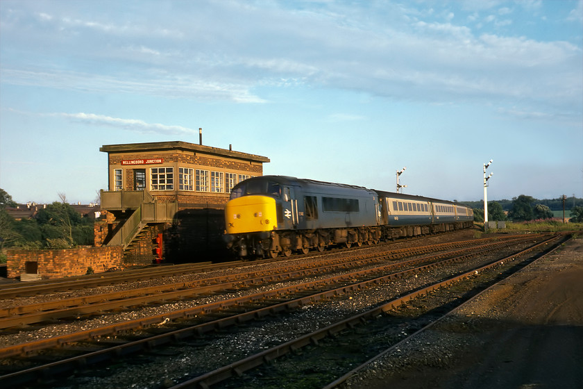 45146, 18.10 London St. Pancras-Nottingham, Wellingborough Junction 
 I am not too sure as to how I had the confidence to get to this spot at Wellingborough Junction a fair way south of the station platform ends? Standing in this location now would put me at the very end of the station's huge and extended car park. The truncated lines off to the right once led the short distance to Wellingborurgh London Road station just near to the Whitworth Mills. Here they joined the line from Peterborough, the western end of which is now part of the Nene Valley Railway, that led westwards to Northampton. If only this line remained open today it would ease the chronic congestion caused by commuters travelling along the A45 to and from Northampton. 45156 is seen leading the 18.10 St. Pancras to Nottingham past the rather austere wartime designed and built signal box dating from 1943. Unfortunately, there is a little motion blur of the Peak spoiling what is otherwise a photograph taken on a perfect late summer evening. 
 Keywords: 45146 18.10 London St. Pancras-Nottingham Wellingborough Junction peak