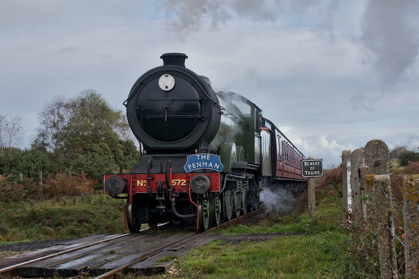 8572, 10.00 Sheringham-Holt, Windpump crossing 
 Having just climbed Kelling bank from a standing start at Weybourne LNER B12 8572 surmounts the summit leading the 10.00 Sheringham to Holt train. The train is wearing a smart headboard as it crosses Windpump crossing on Kelling Heath.

There is an audio recording of this event at my Youtube site, see... https://youtu.be/Ye8gA-D8pQA 
 Keywords: 8572 10.00 Sheringham-Holt Windpump crossing LNER B12 North Norfolk Railway Poppy Line