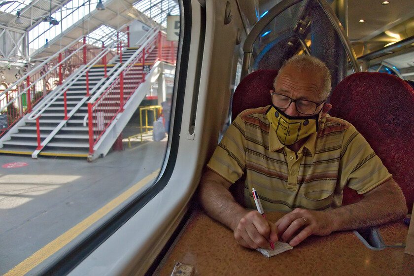 Andy on-board 390122, VT 10.52 Glasgow Central-London Euston (9M54, 5L), Crewe station 
 Andy makes up his notebook as we leave Crewe aboard the 10.52 Glasgow Central to London Euston Pendolino service being worked by 390122 'Penny the Pendolino'. I did not notice until I looked at this photograph when digitally processing it that the bridge has been recently repainted not into Avanti or London Northwestern house colours but those of Transport for Wales. Whilst they are a user of the station they are by no means the most significant so the rationale behind this remains a mystery unless anybody in the know can advise me. 
 Keywords: Andy 390122 10.52 Glasgow Central-London Euston 9M54 Crewe station Penny the Pendolino