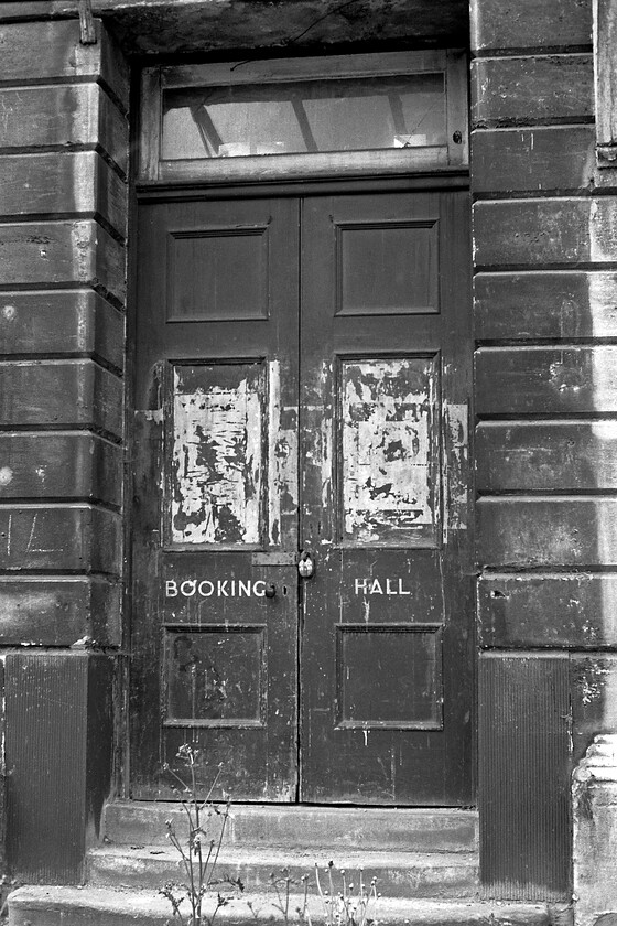 Booking Hall doors, Bath Green Park station 
 The former entrance to Bath Green Park station is taken through wire fencing to keep unwelcome visitors away from the building. After a much-needed redevelopment, this entrance became one of the two for access to the concourse and the interior for the many visitors who now frequent the former station. It looks as though there are lights on in the booking hall but I can assure you that this is strictly an optical illusion of the light outside! 
 Keywords: Booking Hall doors Bath Green Park station