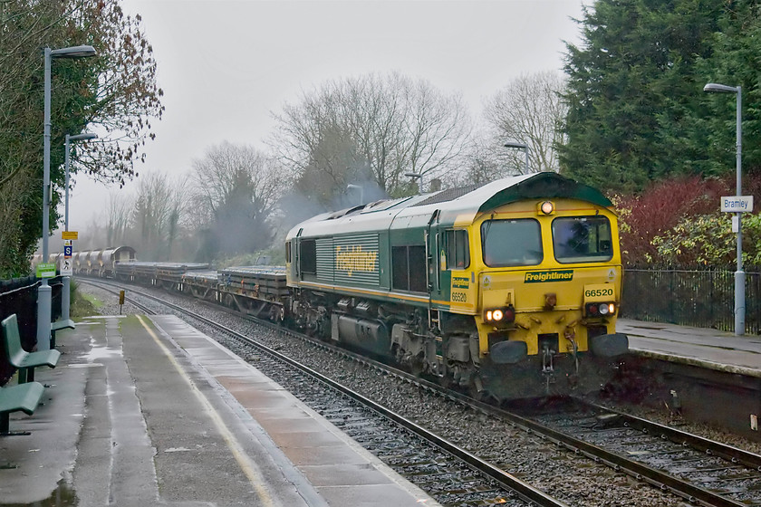 66520, 13.28 Eastleigh Yard-Hinksey Yard (6V27), Bramley station 
 It's twenty-five minutes to three in the afternoon on the shortest day of the year and it's absolutely pouring with rain; please forgive the quality of this photograph! 66520 leads the 13.28 Eastleigh yard to Hinksey yard (Oxford) infrastructure working through Bramley station. Behind the locomotive are five flats carry varying numbers of track panels then further back a rake of loaded ballast wagons. With no more trains due, Andy and I were relieved to be able to return to the Combo van for shelter as there was nothing to protect passengers from the elments on Bramley station! 
 Keywords: 66520 13.28 Eastleigh Yard-Hinksey Yard 6V27 Bramley station Freightliner Infrastructure working