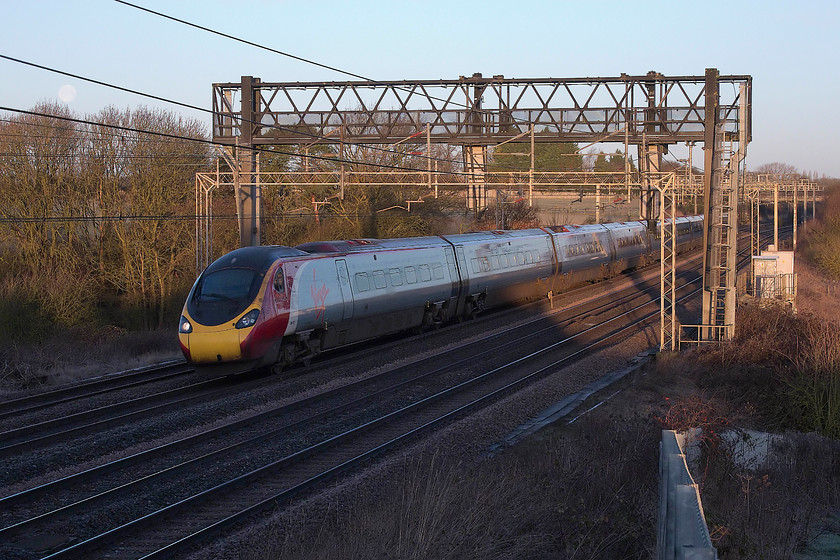 390137, VT 06.58 Manchester Piccadilly-London Euston (1R18, 3L), Roade Hill 
 390137 'Virgin Difference' passes a very cold Roade Hill between Rugby and Milton keynes with the 06.58 Manchester Piccadilly to London Euston. The camera has done well to cope with the extreme tonal range within this picture with only some minor tweaking needed in Photoshop to sort the shadows out. Notice the waning moon just between the wires to the left. 
 Keywords: 390137 06.58 Manchester Piccadilly-London Euston 1R18 Roade Hill