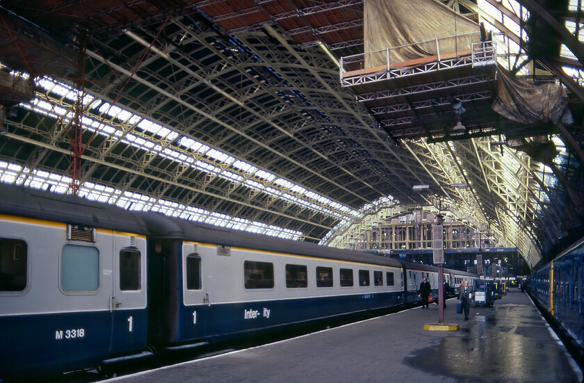 Light restoration, London St. Pancras station 
 Using my wide-angled lens I have taken this interesting interior view of St. Pancras station showing it undergoing some restoration to the frame and glazing. At this time British Rail simply did not have the resources to undertake the full-blown restoration of the vast Barlow designed trainshed hence their efforts very much took a 'finger in the dyke' approach. The 14.07 from Derby has just arrived at platform two whilst a Class 127 DMU waits to leave platform one for Bedford. Notice that some wag has removed the letter C from the branding of the Mk. 2 coach in the foreground perhaps as part of schoolboy attempt to add an erroneous letter T perhaps? 
 Keywords: Light restoration London St. Pancras station