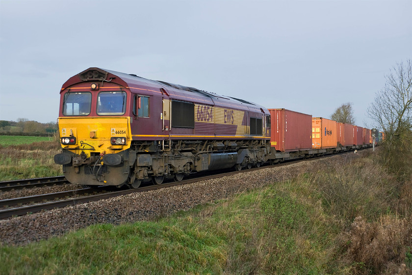 66054, 06.31 Birch Coppice ES-Eastleigh East (4O43), King's Sutton 
 After a very bright start to the day, the sun has been tempered by a huge bank of cloud moving relentlessly in from the northwest. The front of 66054 is still partially illuminated by the weak sun as it passes King's Sutton leading the 06.31 Birch Coppice to Eastleigh East Freightliner train.

There is an audio recording of this event on my youtube channel, see.... https://youtu.be/w4N5Hxh50t0 
 Keywords: 66054 06.31 Birch Coppice-Eastleigh East 4O43 King's Sutton EWS