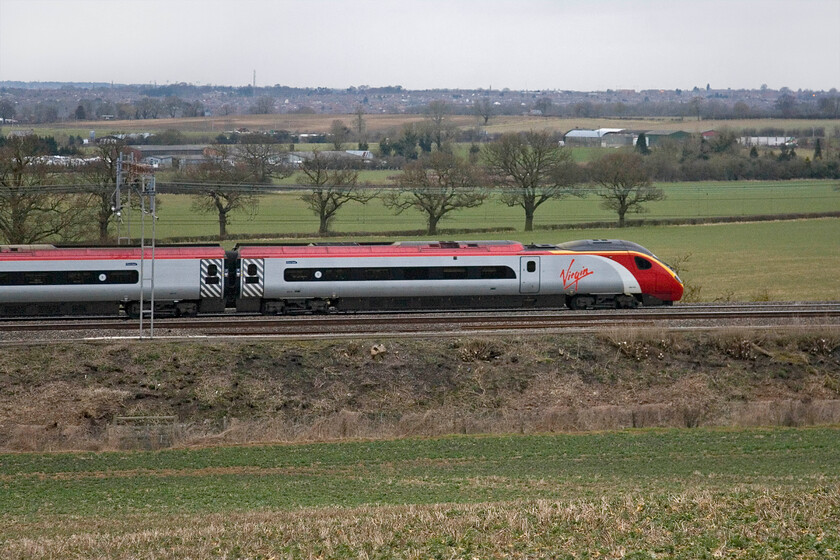 Class 390, VT 06.35 Manchester Piccadilly-London Euston, Blisworth 
 The 06.35 Manchester to Euston service passes Blisworth near Northampton, the town in the background, worked by an unidentified Pendolino. Unfortunately, I have not been able to make out the number of the Class 390 but it certainly adds a flash of colour to an otherwise very dull and flat county scene. 
 Keywords: Class 390 06.35 Manchester Piccadilly-London Euston, Blisworth Virgin Pendolino