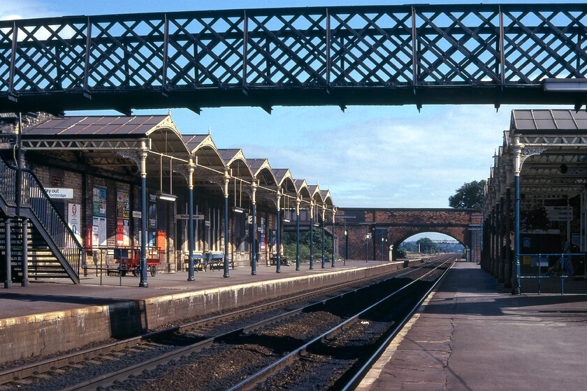 Loughborough station 
 Loughborough Midland, as it was known for many years so as to differentiate it from the GCR station located a short distance away is seen looking south towards Leicester. Whilst its Victorian character is clear in this photograph it is a shame that the canopies have been cut back at some time in the past. Despite this act of architectural vandalism, the station is Grade II listed. Unfortunately, the latched footbridge seen in this view has also been removed to be replaced by a modern monstrosity! Notice how quiet the station platforms are in this early '80s Sunday afternoon view. Today off-peak weekend travel is far more frequent with Sundays becoming noticeably busier than they ever used to be. 
 Keywords: Loughborough station