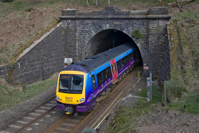 170303, TP 12.26 Cleethorpes-Manchester Airport (1B79), Totley tunnel 
 This was a bit of a grab shot, indeed close examination of 170303 forming the 12.26 Cleethorpes to Manchester Airport service does reveal a little motion blur. However, I like the contrast of the brightly coloured TransPennine Express livery with the dark Millstone Grit tunnel portal and the land surrounding it that has yet to take on any of its spring colours. When the three and a half-mile long Totley Tunnel was opened in 1893, note the engraving above the tunnel mouth, it was the second-longest in the UK behind the Severn Tunnel. Even today it remains the fourth-longest with the two High-Speed one tunnels now being the two longest ones. 
 Keywords: 170303 12.26 Cleethorpes-Manchester Airport 1B79 Totley tunnel