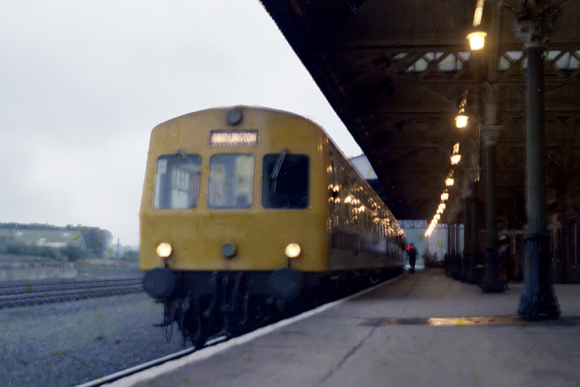 Class 101 DMU, unidentified York-Bridlington working, Malton station 
 A class 101 DMU sits at Malton station with a York to Bridlington working that would reverse at Scarborough. This poor quality image shows Malton station before it was rendered unrecognisable by a re-building programme that involved, almost other things, the removal of the small awning at the far end. 
 Keywords: Class 101 DMU York-Bridlington working Malton station