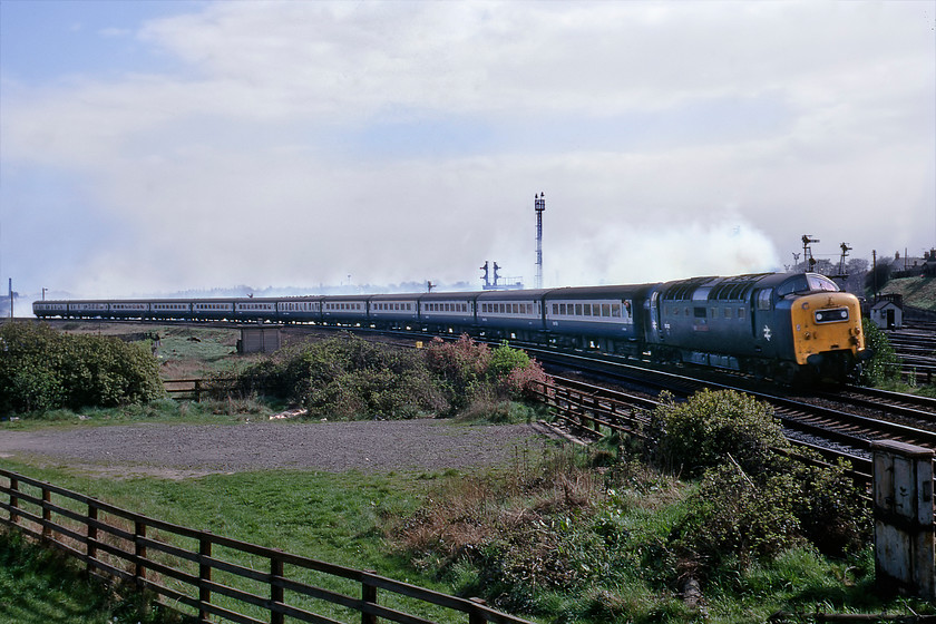 55022, 07.25 Plymouth-Edinburgh (1S25), Water End bridge, York 
 Taken against the sun but a fascinating picture nonetheless! 55022 'Royal Scots Grey' gets away from York picking up speed leading the 07.25 Plymouth to Edinburgh Waverley. Just look at the exhaust trail it is leaving hanging over the northern suburbs of York, with the photograph taken from Water End bridge. The twin Napiers were always a little smoky but especially so until fully warmed up and this example would have been running still fairly cool, having just taken over the train at York station about a mile away. It would also have been at full power getting the train up to line speed for the racetrack between York and Northallerton. Also of interest is the number of semaphore signals behind the train controlling the extensive sidings and York avoiding lines. Looking at Google Earth reveals that this scene is little changed today except for some tree growth to the left and the installation of the electrification equipment.

There is an audio recording of this event on my youtube channel, see.... https://youtu.be/ndJyHiTrEms 
 Keywords: 55022 07.25 Plymouth-Edinburgh 1S25 Water End bridge York Royal Scots Grey Deltic