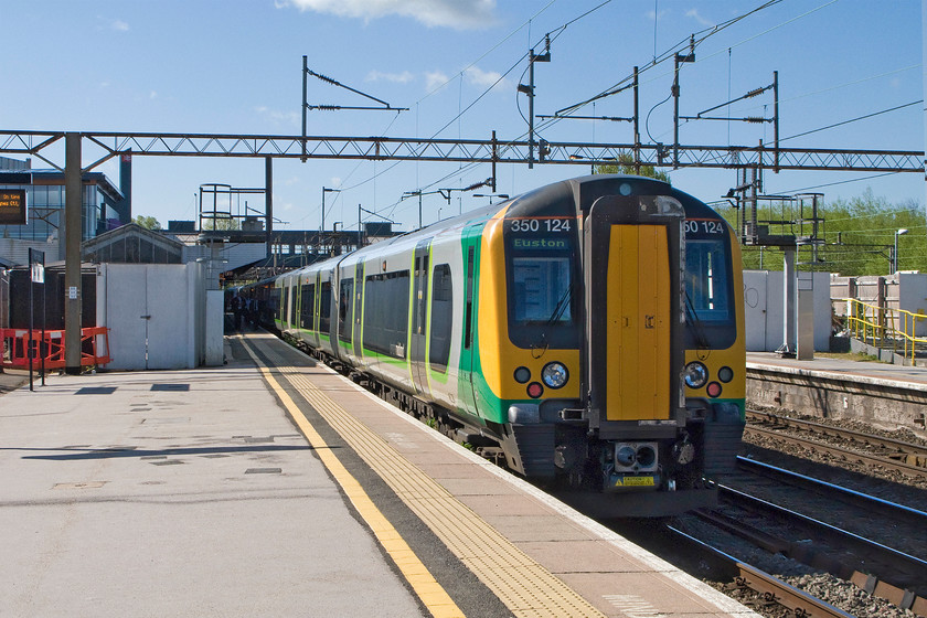 350124, LM 08.33 Birmingham New Street-London Euston (1W06), Northampton station 
 350124 pauses at Northampton station forming the 08.33 Birmingham New Street to Euston 1W06 service. The white doors to the left and the yellow railings to the right mark the location of the gargantuan temporary footbridge that was installed by Network Rail whilst the old one was demolished and the new one built, seen in the background above the roof of the Desiro. 
 Keywords: 350124 08.33 Birmingham New Street-London Euston 1W06 Northampton station Desiro London Midland Railway