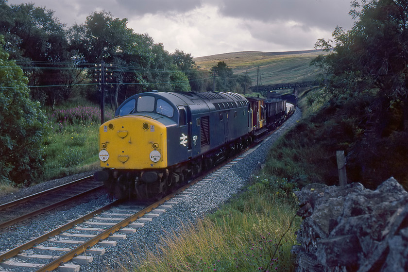 40011, down freight, Ais Gill, SD773979 
 In rather dull and dismal conditions, 40011 leads a classic mixed freight northwards on the descent from Ais Gill summit passing Angreholme. Just look at the incredible collection of wagons behind the brake van. It is trains such as this that were disappearing from our railways at this time but that I took precious few photographs of. As D211 'Mauritania' the locomotive entered service in May 1959 (twenty-one years prior to this photgraph being taken) but had just six weeks left in service being withdrawn early in October 1980. I photgraphed 40011 during its last visit to Crewe Works, see.... https://www.ontheupfast.com/p/21936chg/26146599604/x47182-40011-crewe-works 
 Keywords: 40011 down freight Ais Gill, SD773979