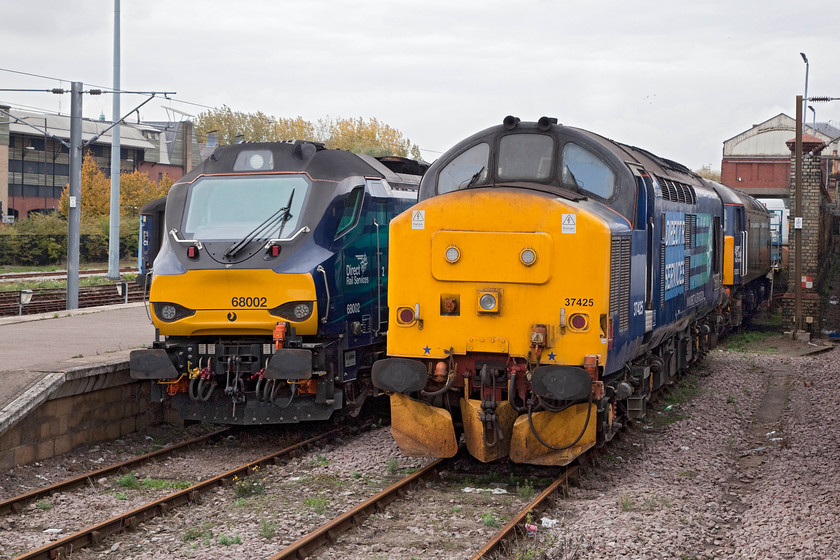 68002, 37425 & 57303, stabled, Norwich yard 
 Taken from the open window of a London train waiting in platform one at Norwich station is a trio of DRS' finest! To the left is 68002 'Intrepid', then 37425 'Concrete Bob' and finally tucked away at the back is 57303 'Pride of Carlisle'. The locos. are all stabled waiting for work running the Greater Anglia services covering for their persistent DMU shortages. Every year the railway press state that this is the last season of these workings but, they keep being retained....for how long one wonders? 
 Keywords: 68002 37425 57303 Norwich yard