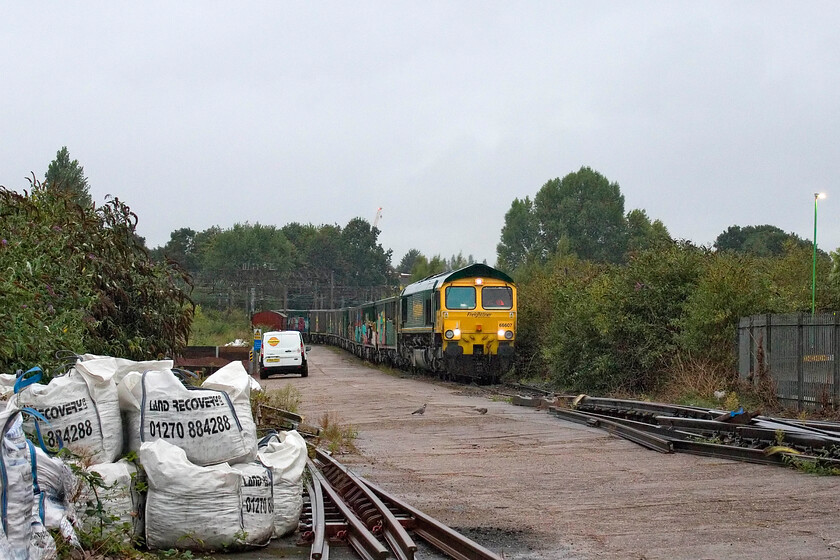 66607, 00.51 Tunstead Sidings-Northampton Castle Yard (6B30, 38E), Northampton station car park 
 Regular stone trains have become a feature of Northampton Castle Yard with daily trains, sometimes twice a day, delivering crushed stone of various grades and types into the virtual quarry which is also on-site. The deliveries of the vast amounts of stone are associated with the construction of HS2 with regular lorry movements to and from the various work sites a bit of an issue to the western side of Northampton. 66607 has brought the 00.51 Tunstead to Castle Yard working in and is involved in some convoluted shunting that involves the wagons being split for unloading before the whole train returns north again later in the morning. The photograph is taken through the gates from the station car park. 
 Keywords: 66607 00.51 Tunstead Sidings-Northampton Castle Yard 6B30 Northampton station car park Freightliner