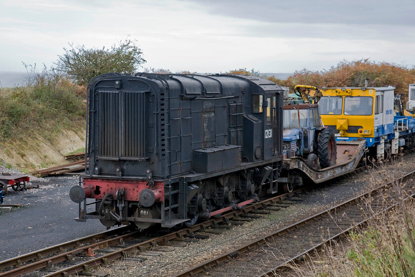 12131, stabled, Weybourne yard 
 With a very grey North Sea in the background 1952 built Class 11 shunter 12131 sits stabled in Weybourne's yard. Notice the rather aged Ford tractor sitting on the low loader behind the shunter. The tractor is used along the length of the line to cut the embankments with its extending arm in an effort to reduce lineside problems, Network Rail please take note! 
 Keywords: 12131 Weybourne yard