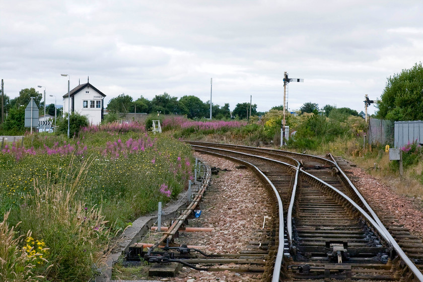 Forres signal box (McK&H & High, 1896) from Waterford level crossing 
 Taken from Waterford level crossing that is controlled by Forres signal box the main Aberdeen to Inverness line is seen curving away to the left and Forres station just a short distance away. The stub of track going straight ahead used to lead to the yard that is now completely overgrown. Plans have just been announced that a new station is to be built at Forres and the track realigned probably straight ahead to avoid the sharp curve into the present station. The semaphores and lovely 1896 McKenzie and Holland Highland box will be swept away when all this takes place over the coming few years. 
 Keywords: Forres signal box Waterford level crossing McKenzie & Holland Highland box