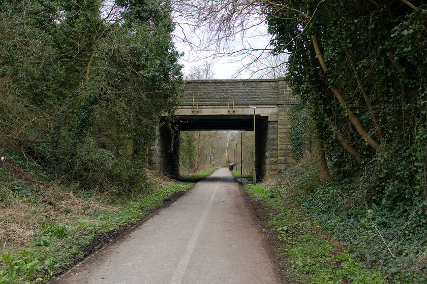 B573 Ovangle Road, from route of Green Ayre Railway, Morecambe 
 To collect my new car I walked from Lancaster station to the dealership on the eastern side of Morecambe. This walk involved a walk along part of the Sustrans Route 69 that followed the route of the former Green Ayre Railway. The story of this line is a fascinating one that revolves around the construction of the world's first overhead electrified line initially utilising 6,600 volts. This pioneering line that ran from Lancaster to Morecambe was set up by the Midland Railway and used as a test bed for further electrification methods later adopted on the wider network. In its later life, after the wiring was removed, it became a forgotten outpost with it closing in 1966 with intermittent freight operating until 1976. The bridge seen in this scene carries Ovangle Road over the former line. I wonder if the four vertical steel tubes attached to the bridge are a remnant of the electrification equipment? 
 Keywords: B573 Ovangle Road from route of Green Ayre Railway Morecambe