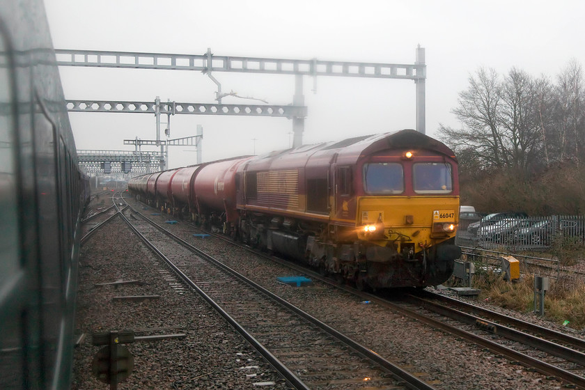 66047, 13.00 Theale-Robeston Sidings (6B33), Swindon Down Yard 
 Andy and I had been waiting at Swindon for the daily 6B33 Theale to Robeston oil train to pass but, unfortunately it was late. So, our train passed it just outside Swindon while it was looped in the Down Yard. Also, to add to our disappointment, it was headed by 66047 rather than the more usual class 60. A droplight window shot from our train sees the working waiting patiently in the rain for the road. 
 Keywords: 66047 13.00 Theale-Robeston Sidings 6B33 Swindon Down Yard