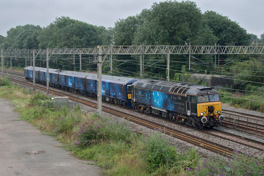 57312 & 768001, 08.44 Wembley HS-Hams Hall (5Q66, RT), site of Roade station 
 Orion has ambitious plans to transport smaller freight items between, initially at least, Glasgow and Euston. It has been undertaking many test runs and filming a slick promo as part of the launch, see.... https://www.youtube.com/watch?v=E9TCt8pMS4s A daylight test run is seen passing through Roade as the 5Q66 08.44 Wembley Yard to Hams Hall with 768001 being towed by 57312. The unit is a former Thameslink unit 319010 that has been completely stripped and fitted out to carry small freight items that are moved on integrated trolleys. 
 Keywords: 57312 768001 08.44 Wembley HS-Hams Hall 5Q66 site of Roade station Orion Logistics