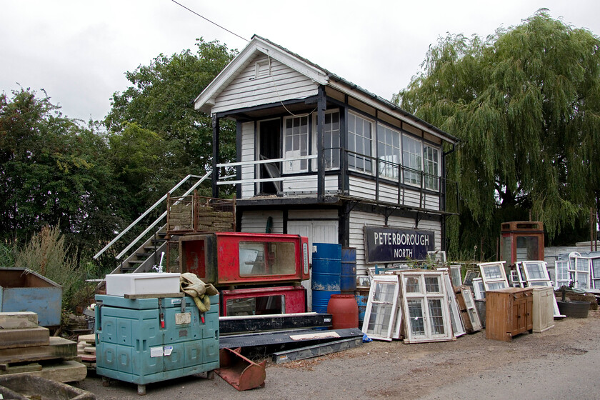 Former Horsemoor signal box, at Murrow West (GE, 1899) 
 I last photographed this signal box at its original location to the East of March where the B1099 crosses the Ely line back in the summer of 1981, see...... https://www.ontheupfast.com/p/21936chg/30046908461/horsemoor-signal-box-great-eastern. Horsemoor box is a Great Eastern Type 7 design dating from 1899 distinguished by the roofed landing and the single horizontal crossbar glazing to the front windows. It was closed in the autumn of 1988 and was bought and moved to this site in a reclaim yard at Murrow West situated now on the Peterborough side of the M & GN line that crossed the GN & GR Joint line just behind where I am standing. On balance, the large Peterborough North enamel attached to the front is probably the original sign from that box that was closed in 1972. However, I have struggled to find any contemporary photographs of that box sporting the sign so its providence cannot be assured. 
 Keywords: Former Horsemoor signal box Murrow West GE