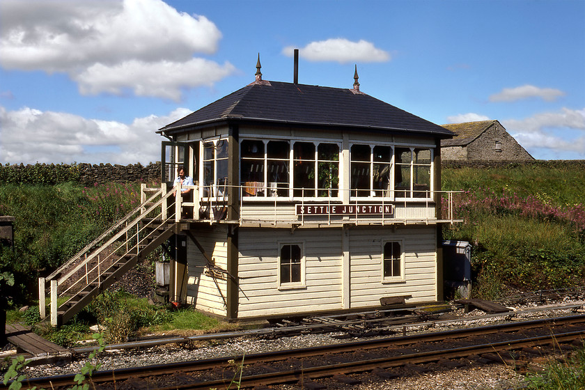 Settle Junction signal box (Midland, 1913) 
 I took a photograph of Settle Junction signal box during a passing visit last summer but on that occasion, it was late in the day and the light was totally wrong. Our visit on this day was in the morning with the sun illuminating the front of the lovely Midland box dating from 1913. The signalman can be seen taking in the sun at the top of the steps but don't be fooled by this seemingly bucolic scene, directly behind me is the busy A65 Kendal to Leeds road. As of 2020 the box still exists and is in use controlling semaphores that were photographed during my most recent visit in 2018, see...... https://www.ontheupfast.com/p/21936chg/24425937604/x158784-2h89-settle-junction-sd813606 In addition, I also visited the box in 2014 (almost thirty-four years to the day) and took a very similar photograph apart from the growth of the trees, see..... https://www.ontheupfast.com/p/21936chg/30016458766/x12-settle-junction-signal-box-mr. I wonder if the signalman mentioned earlier is still working on the railways? 
 Keywords: Settle Junction signal box Midland Railway MR