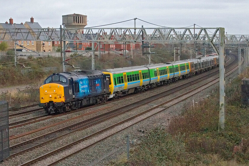 37800, 323221, 323211 & 323214, 13.05 Wolverton Centre Sidings-Long Marston (5Q95, 39L), site of Roade station 
 This train was worth keeping an eye on and leaving my lunch steaming on the kitchen table for! Leaving from Wolverton Works being only a few miles south of Roade gives little warning of its departure so when the reporting number appears on RTT it's time to get on the bike and nip down to the track! 37800 'Cassiopeia' leads a colourful ensemble composed of celebrity retro. Regional railways liveried 323221 followed by 323211 and 323214 running as the 5Q95 13.05 Wolverton Works to Long Marston. With the ending of Class 323 operations throughout the West Midlands a few months ago some units headed north to Northern whilst others went to Wolverton for various works and are now heading off to storage and a very uncertain future. Being extremely reliable units, there has been some interest in future use, but they are now thirty years old! 
 Keywords: 37800 323221 323211 323214 13.05 Wolverton Centre Sidings-Long Marston 5Q95 site of Roade station Cassiopeia