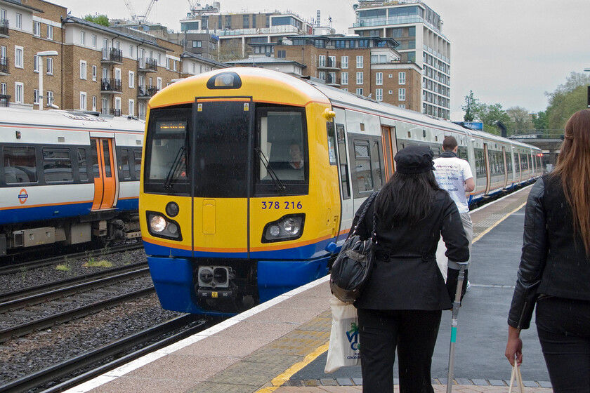 378216, LO 16.01 Clapham Junction-Willesden Junction High Level, Kensington Olympia station 
 Passengers brave the rain as they walk from the station shelter to their train at Kensington Olympia, the 16.01 Clapham Junction to Willesden Junction High level worked by 387216. It's sobering to think that my first visit to this London station was thirty-two years ago almost to the day, see.... https://www.ontheupfast.com/p/21936chg/30022860822/x33016-50015-unidentified-light-engines 
 Keywords: 378216 16.01 Clapham Junction-Willesden Junction High Level Kensington Olympia station Capitalstar London Overground