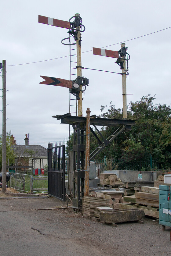 Home bracket signal, Murrow West 
 When I visited Murrow West back in 1981 I have it noted in my book that I saw a disused bracket signal to the west of Murrow signal box but that it had no arms. The arms have now been added by the owner of the reclaim yard in which the bracket is sited. The home and distant doll controlled the M & GN single-track route from Peterborough (behind me) to Wisbech that crossed the GN & GR Joint line on a flat crossing just beyond the former railway cottage on the left. The single home permitted trains to pass from the M & GN south on to the GN & GR route via short and tight spur. This was added late in 1961 to permit bricks to be taken by rail from the Eye and Dogsthorpe brickworks for onward transportation from Whitemoor Yard following the closure of the rest of the Peterborough to Wisbech line. This operation did not last long with the complete closure of the M & GN rote coming in 1966. 
 Keywords: Home bracket signal Murrow West