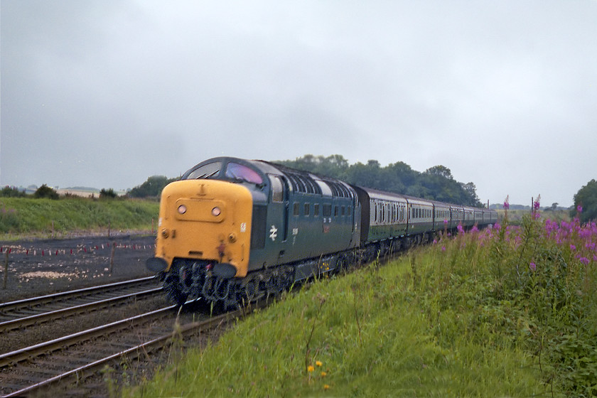 55018, 10.55-Leeds-London Kings Cross (1A14), High Dyke SK942289 
 55018 'Ballymoss' is about to complte its climb of Stoke Bank as it enters the tunnel a short distance behind the camera. It is working the 1A14 10.55 Leeds to King's Cross. In the background can be seen the bare area of ballast and clinker that used to be home to the extensive sidings at High Dyke. These concentration sidings were used to marshall wagons that carried ironstone from a number of open cast mines alongs the line built to the south towards Colsterworth. 
 Keywords: 55018 10.55-Leeds-London Kings Cross 1A14 High Dyke SK942289