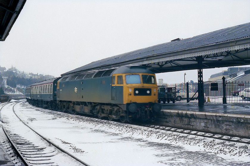 47104, unidentified up working, Bath Spa station 
 47104 arrives into Bath Spa station with an unidentified up working. As there was some weather related disruption on this day, the identification of workings was tricky. However, the restaurant car located directly behind the loco. may indicate that it originated somewhere in the west country as this was a feature of their formations. Apologies for the motion blur but the Exa camera's maximum shutter speed of 1/150 sec. was pretty useless. What is also of interest are the cars in the station car park, the most recognisable being the white Mk. I Capri with a natty vinyl roof! 
 Keywords: 47104 unidentified up working Bath Spa station