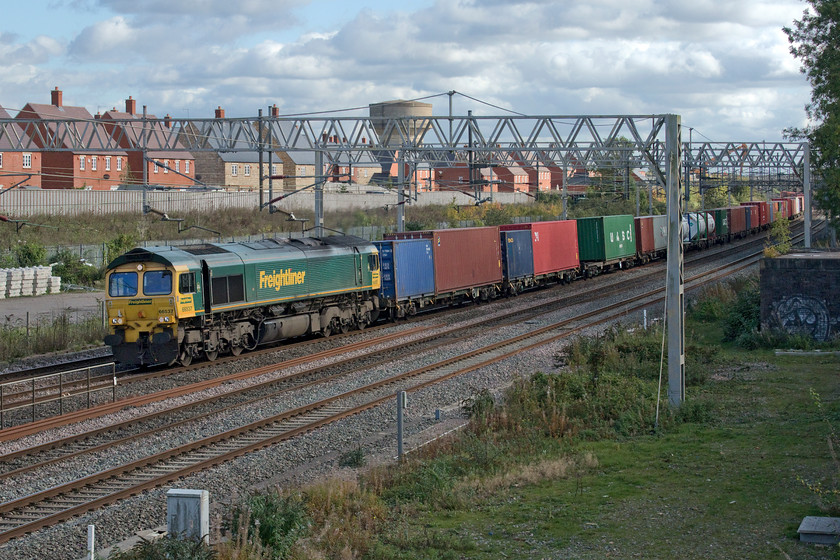 66537, 09.25 Southampton MCT-Garston (4M28, 14E), site of Roade station 
 As is all too common with our hobby the sun often dives behind a cloud at the crucial moment to coincide with the passage of a particular train! With the new houses in the background that occupy the former Pianoforte site and the rear of the train bathed in lovely October sunshine, the 09.25 Southampton to Garston Freightliner, led by 66537, is in the shade! This working is a strange one and I have never quite understood why it is routed via the busy WCML rather than the more normal Oxford and Banbury route. Explanation anybody? 
 Keywords: 66537 09.25 Southampton MCT-Garston 4M28 site of Roade station Freightliner