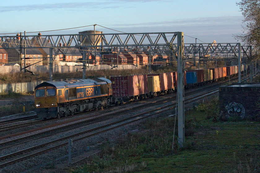 66765, 10.36 Felixstowe N-Hams Hall (4M23, 44L), site of Roade station 
 It's not even 15.00 and the sunlight has all but abandoned me at Roade! Working well GBRf's 66765 brings the well-loaded 4M23 10.36 Felixstowe to Hams Hall past the site of the village's former station. With the upgrading of the Ely to March and Peterborough to Leicester routes it is these sort of workings that will move away from the WCML easing congestion on what is the busiest route on the UK's network. However, will COVID change things forever? We'll see over the coming six months or so! 
 Keywords: 66765 10.36 Felixstowe North-Hams Hall 4M23 site of Roade station GBRF