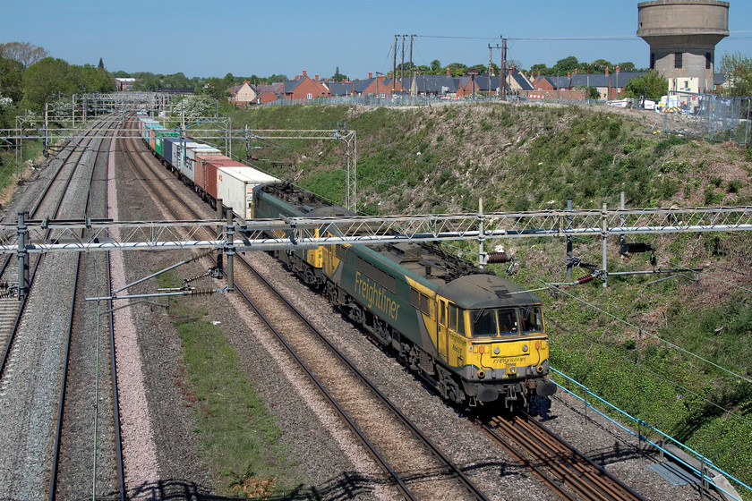 86637 & 86605, 05.00 Trafford Park-Felixstowe North (4L75, 2E), Ashton Road bridge 
 86637 and 86605 lead the 05.00 Trafford Park to Felixstowe Freightliner past Ashton Road bridge just south of Roade on another stunning spring day. One of Roade's two water towers, currently being converted into a residence, is seen dominating the horizon to the right. This is not a great spot for capturing a double-headed train with the electrification equipment spoiling the view somewhat! However, Class 86s should be photographed on every occasion at the moment due to their probable and imminent demise! 
 Keywords: 86637 86605 05.00 Trafford Park-Felixstowe North 4L75 Ashton Road bridge Freightliner AL6