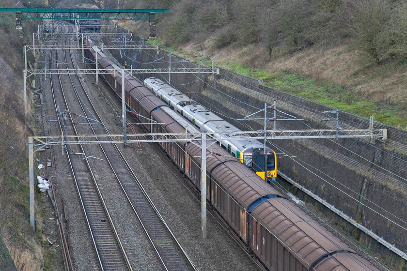 350266, LM, 12.15 Birmingham New Street-London Euston (1Y40) & 11.47 Wembley-DIRFT (0B41), Roade cutting 
 The diminutive size of London Midland's 350266 working the 12.15 Birmingham to Euston service is clear in the scene in Roade cutting. It is somewhat dwarfed not only by the size of the cutting but also by the cargo wagons carrying bottled water from Wembly to Daventry. The 0B41 is being hauled by 92036 'Bertolt Brecht' that is already well out of sight at the front of the train. 
 Keywords: 350266 12.15 Birmingham New Street-London Euston 1Y40 11.47 Wembley-DIRFT 0B41 Roade cutting London Midland Desiro