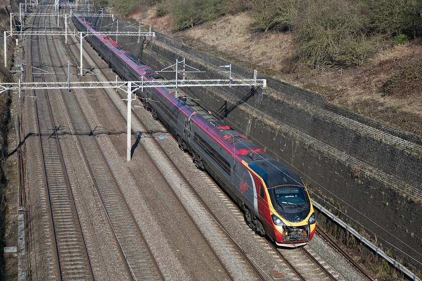 Class 390, VT 09.20 Manchester Piccadilly-London Euston, Roade cutting 
 Another example of a Pendolino working with its front drawbar cover wide open which seems to be a regular occurrence at the moment. As well as doing nothing for aerodynamics it will also mean any poor creatures that are hit by the train will get drawn into the area that is full of much-complicated equipment. I for one would not fancy the job of pulling the remains out at a depot in the evening! The unidentified Class 390 heads south through Roade cutting working the 09.20 Manchester to Euston service that has been routed via Northampton rather than via the mainline due to engineering work. 
 Keywords: Class 390 09.20 Manchester Piccadilly-London Euston Roade cutting Virgin Pendolino