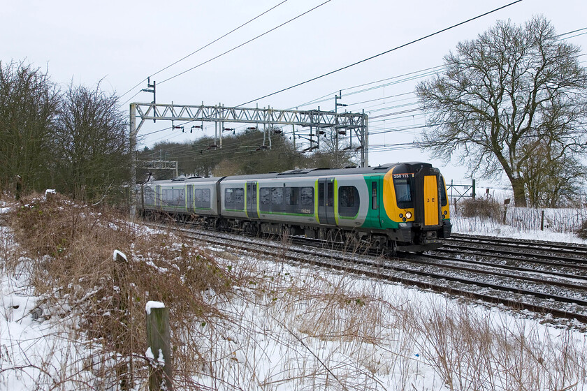 350113, LM 09.46 London Euston-Crewe 
 Probably pretty empty by this time in the day after running south to London packed with commuters earlier in the morning, London Midland's 350113 passes Roade working the 09.46 Euston to Crewe service. Having been standing in a snowy field on crutches for some time now it felt like I ought to be heading for home a relatively short trek across the filed behind me. 
 Keywords: 350113 09.46 London Euston-Crewe London Midland desiro