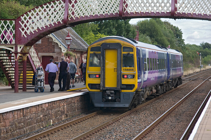 158855, NT 15.05 Carlisle-Leeds (1E23), Appleby station 
 A busy scene at Appleby station as the 15.05 Carlisle to Leeds pauses on its journey south. The train was very crowded as it passed me standing on the platform that begs the question as to whether a two-car 158855 was sufficient for such a service during high summer? Notice the refreshment trolley that is about to be loaded on to the train via the ramp but I am not too sure how easily it would be able to move around the train given how busy it was! 
 Keywords: 158855 15.05 Carlisle-Leeds 1E23 Appleby station