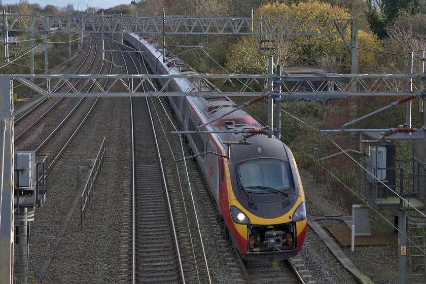 390137, VT 14.00 London Euston-Manchester Piccadilly (1H29), site of Roade station 
 390137 passes Roade on the down fast line with the 1H29 Euston to Manchester Piccadilly service. Despite the pedestrian bridge spanning the entire four lines at this location, opportunities for reasonable photographs is somewhat limited in part due to rampant and extensive lineside vegetation. 
 Keywords: 390137 14.00 London Euston-Manchester Piccadilly 1H29 site of Roade station Virgin Pendolino