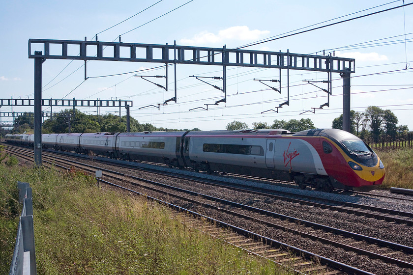 390128, VT 13.03 London Euston-Birmingham New Street (9G22), passing the TSR, Ashton Road bridge 
 390128 'City of Preston' passes between Ashton and Roade on the WCML just across the filed from my home. This is an everyday scene and not one that I would normally capture like this, the wrong side of the sun. However, a shutter speed of 1/400th sec. is all that was needed to capture this train, normally I would use 1/1600th sec. This was because all up and down fast services were at walking pace past this location due to re-ballasting taking place the previous night following track repairs. The tamping had not been completed being finished over the night to come. 
 Keywords: 390128 13.03 London Euston-Birmingham New Street 9G22 passing the TSR, Ashton Road bridge