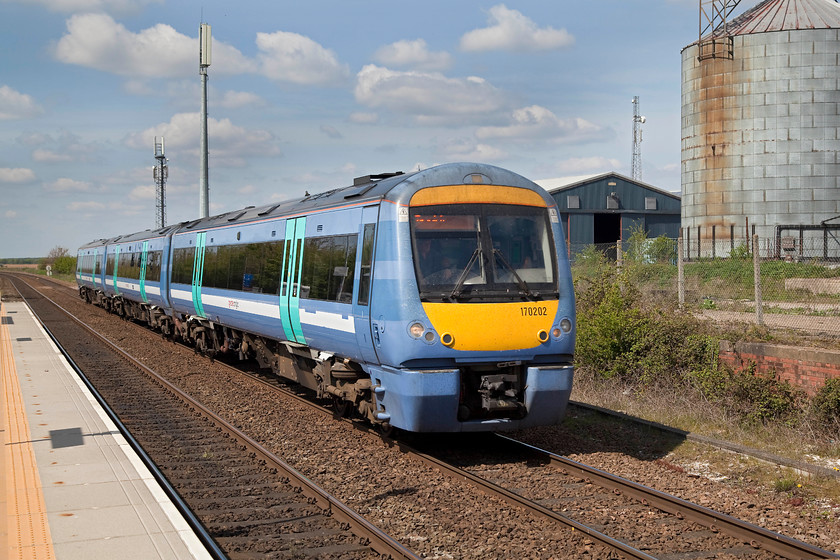 170202, LE 11.44 Cambridge-Ipswich (2W15, RT), Kennett station 
 170202 passes through Kennett station working the 11.44 Cambridge to Ipswich service. In the background is a large grain silo that marks the sight of of the former rail served granary. A Speedlink service operated into the granary up until the 1980s. Whilst theis scene looks to be a tranquil rural scene, looks can be deceiving as the A14 trunk road thunders past the station behind where I am standing taking the picture! 
 Keywords: 170202 2W15 Kennett station