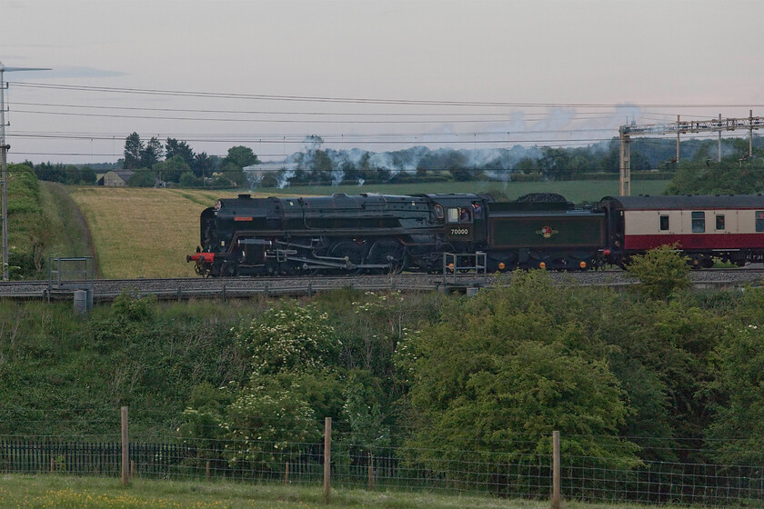 70000, return leg of The Royal Charter, 18.13 Windsor & Eton Riverside-Crewe (1Z70, 3L), Roade Hill 
 In the half-light of a summer's evening 70000 'Britannia' returns north along the WCML leading the 1Z70 Royal Charter. The train had left Windsor and Eton Riverside at 18.13 returning to Crewe. The setting sun was tantalisingly close to illuminating this view between the villages of Roade and Ashton with a stubborn veil of cloud obscuring it! 
 Keywords: 70000 The Royal Charter 18.13 Windsor & Eton Riverside-Crewe 1Z70 Roade Hill Class 7 Saphos Trains