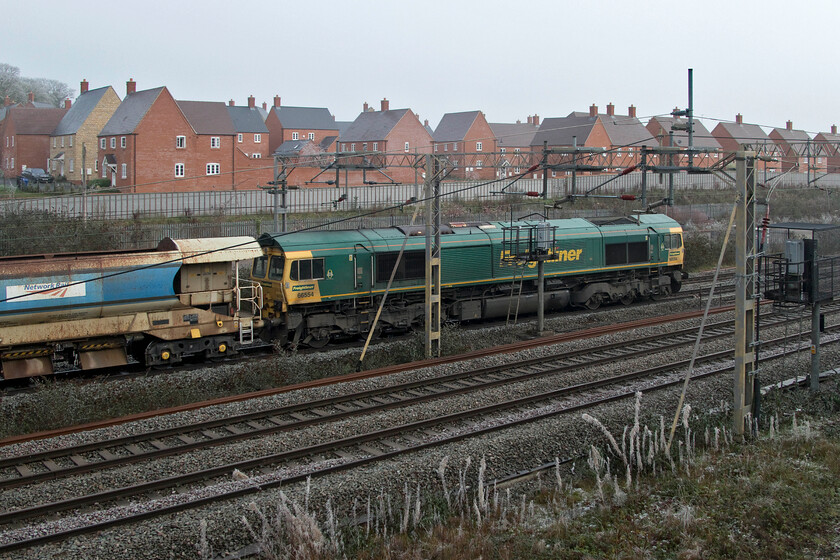 66554, 11.33 Hanslope Junction-Bescot Yard (6Y61, 9L), site of Roade station 
 Dead in tow at the back of the train 66554 passes the site of Roade's former station. The HQAH autoballaster gives a clue as to the working, the 6Y61 11.33 Hanslope Junction to Bescot Yard infrastructure train following from overnight work near Bletchley in association with the East-West railway. 
 Keywords: 66554 11.33 Hanslope Junction-Bescot Yard 6Y61 site of Roade station Freightliner