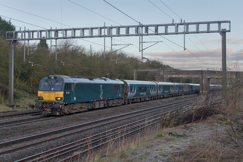 92033, CS 20.26 Inverness, 21.12 Aberdeen, 19.00 Fort William-London Euston (1M16, 2L), Ashton Road bridge 
 92033 leads the Highland Sleeper just south of Roade in Northamptonshire. With the mornings getting a little lighter and with the prospect of a sunny morning I ventured out to see this working but the sun did not play ball hiding behind a stubborn bank of cloud. The Sleeper services are going through a period of increased reliability in recent months following the disastrous introductory period of the Mk.IV stock. 
 Keywords: 92033 20.26 Inverness 21.12 Aberdeen 19.00 Fort William-London Euston 1M16 Ashton Road bridge Caledonian Sleeper