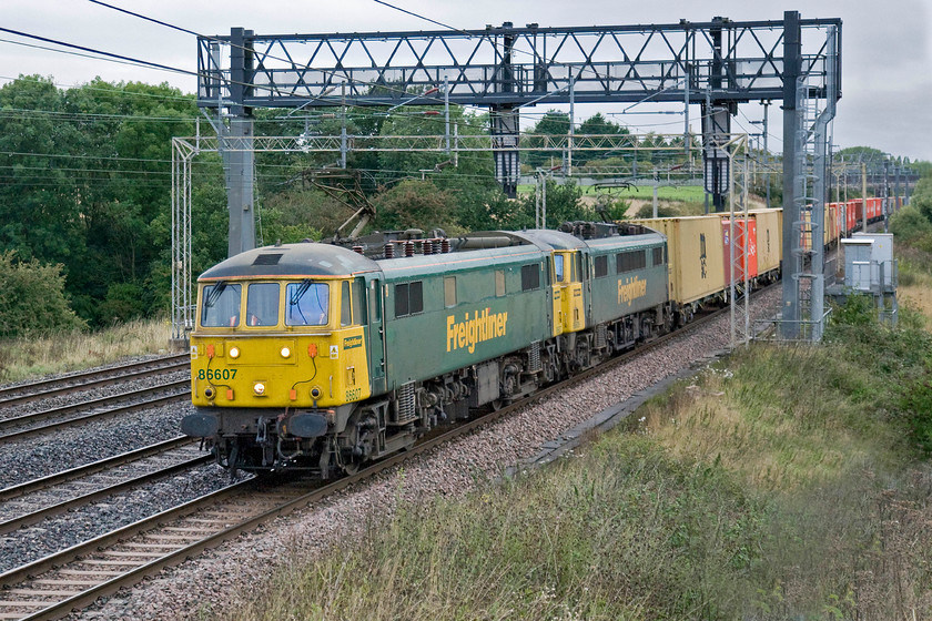 86607 & 87609, 04.10 Crewe Basford Hall-Felixstowe North (4L89), Roade Hill 
 86607 and 86609 lead the 4L89 04.10 Crewe Basford Hall to Felixstowe Freightliner past Roade Hill just south of the village of the same name. The use of these vintage ac electrics continues despite increasing unreliability but there is a dearth of other modern and reliable locomotives so they are set to be about for little longer yet. 
 Keywords: 86607 87609 04.10 Crewe Basford Hall-Felixstowe North 4L89 Roade Hill al1 Freightliner