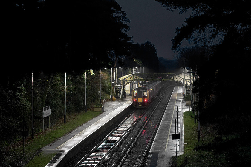 450033, SW 13.39 London Waterloo-Bournemouth (2B39, RT), Sway station 
 I really like the atmosphere conveyed by this image that is somewhat of a surprise as it was a grab shot taken in the pouring rain using the parapet of the bridge to steady the camera. The image shows 450033 standing at Sway station working the 13.39 Waterloo to Bournemouth service. Sway is a small village in the middle of the New Forest just west of Brockenhurst ninety-five miles from Waterloo. Notice the ominous and somewhat sinister dark shapes of the trees towering above the station contrasting with the clear white illumination from the station's LED lighting. Also, note that the modern lighting directs all of its lumens downwards with very little escaping into the night sky thus not contributing towards the scourge of light pollution. 
 Keywords: 450033 13.39 London Waterloo-Bournemouth 2B39 Sway station New Forst South Western Railway SWR