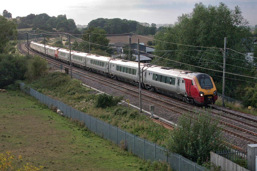 221109 & 221108, VT 18.30 Birmingham New Street-London Euston (1D80, 26L), Banbury Lane bridge 
 After a belting hot day (the warmest August day since 2003) the cloud has really built and all but obliterated the sun which is a good thing here on Banbury Lane bridge as this view would be strongly backlit had it been out. 221109 and 221108 head south working the 18.30 Birmingham to Euston service. In the middle distance level with the third coach there was a level crossing and, until September 1988, a lovely and somewhat remote LNWR signal box. After the closure of the box, the crossing was converted to an automated CCTV version monitored by Rugby PSB, that survived for a few years to be replaced by the larger bridge on which I am standing with an associated road diversion that opened in 2004. 
 Keywords: 221109 221108 VT 18.30 Birmingham New Street-London Euston 1D80 Banbury Lane bridge Avanti West Coast Voyager