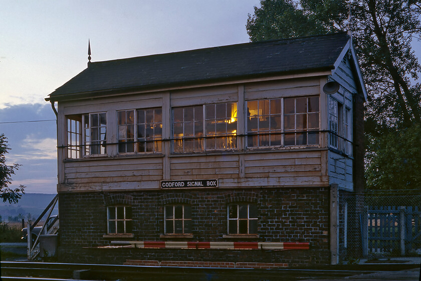 Codford signal box (GW, date unknown) 
 The interior lights just beginning to glow inside the box and with the sun setting fast on this summer's evening a very atmospheric photograph is presented of Codford signal box. I do not have a date for the box's construction by the GWR but it is of a type built between 1889 and 1896 characterised by a simpler window bar arrangement and a slightly shallower hipped roof. In this view, it is good to see the GWR cast plate still attached to the front of the box and it retaining its pair of finials. The box was to close in just under a year on 07.06.82. 
 Keywords: Codford signal box GWR Great Western Railway